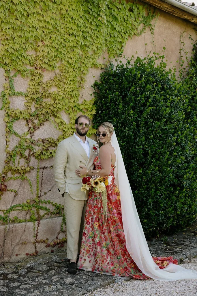 Bride and groom in floral gown and linen suit against ivy and stone