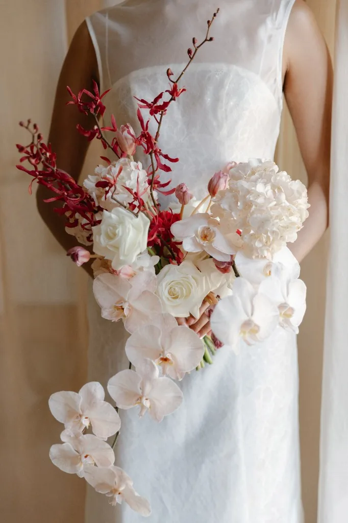 Bride holding a cascading bouquet of white orchids and red flowers