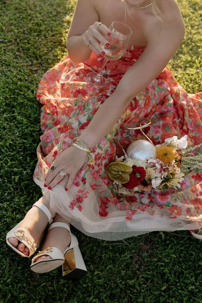 Sydney & Julien, Casale del Gallo, Rome: bride in floral skirt on the lawn with wine glass and bouquet detail