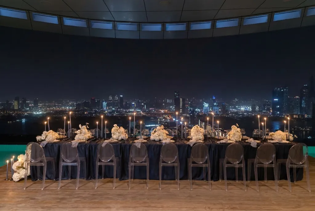 Rooftop dinner at night: candlelit table with white florals and city lights beyond